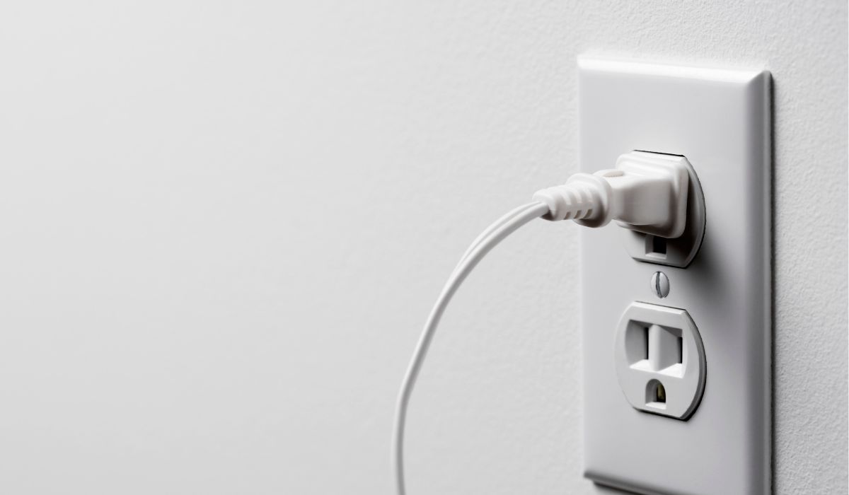 an eletrical safety outlet in a white wall with a white cord plugged in